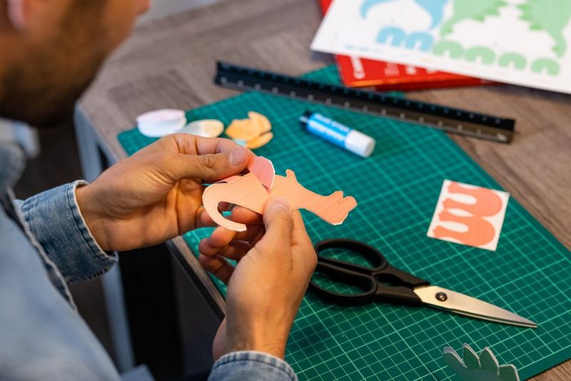 Мужчина прикрепляет ноги к оранжевому бумажному динозавру.