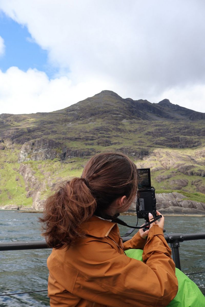 Vlogerka Niam Mekinon snima video pomoću fotoaparata Canon EOS R50 V, gledajući preko jezera ka brdima na ostrvu Skaj.