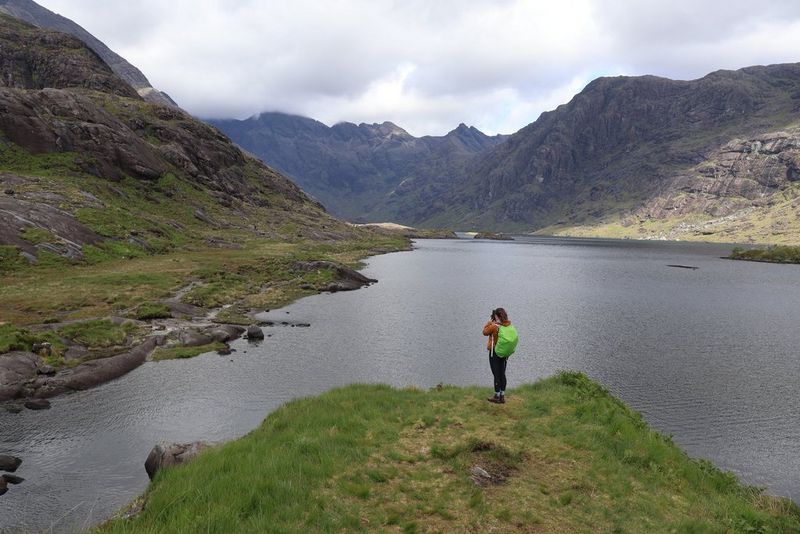 Vlogerka Niam Mekinon stoji i gleda na jezero u brdima na ostrvu Skaj, snimajući video pomoću fotoaparata Canon EOS R50 V.