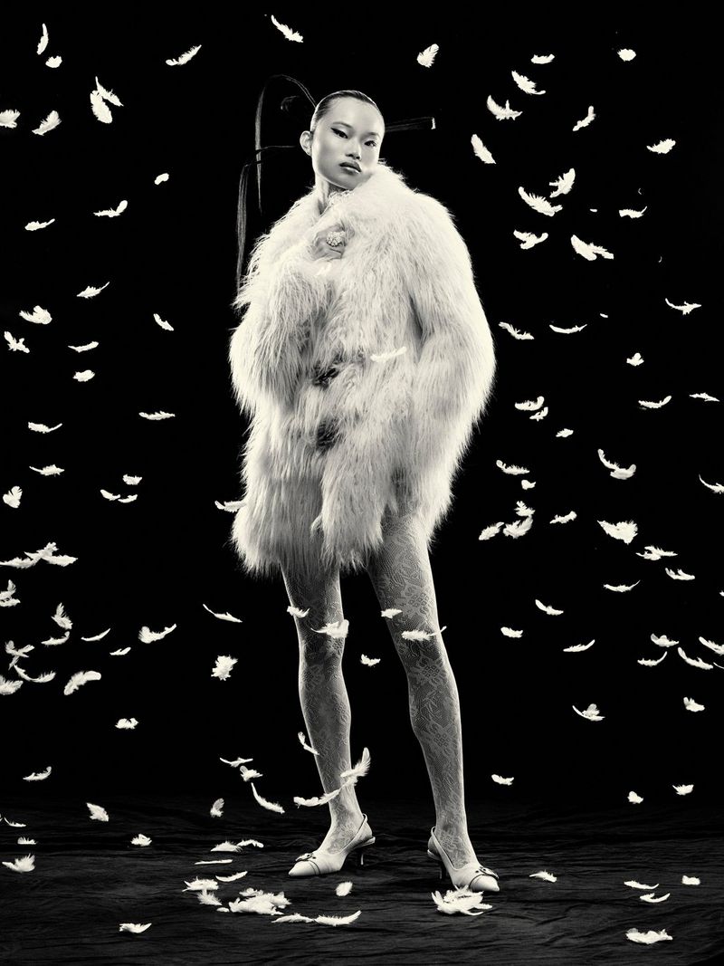 Crno-bijeli modni portret ženskog modela u kratkom kaputu s perjem, okruženog perjem koje pada oko nje. Snimio Ian Hippolyte modelom EOS R5 tvrtke Canon.