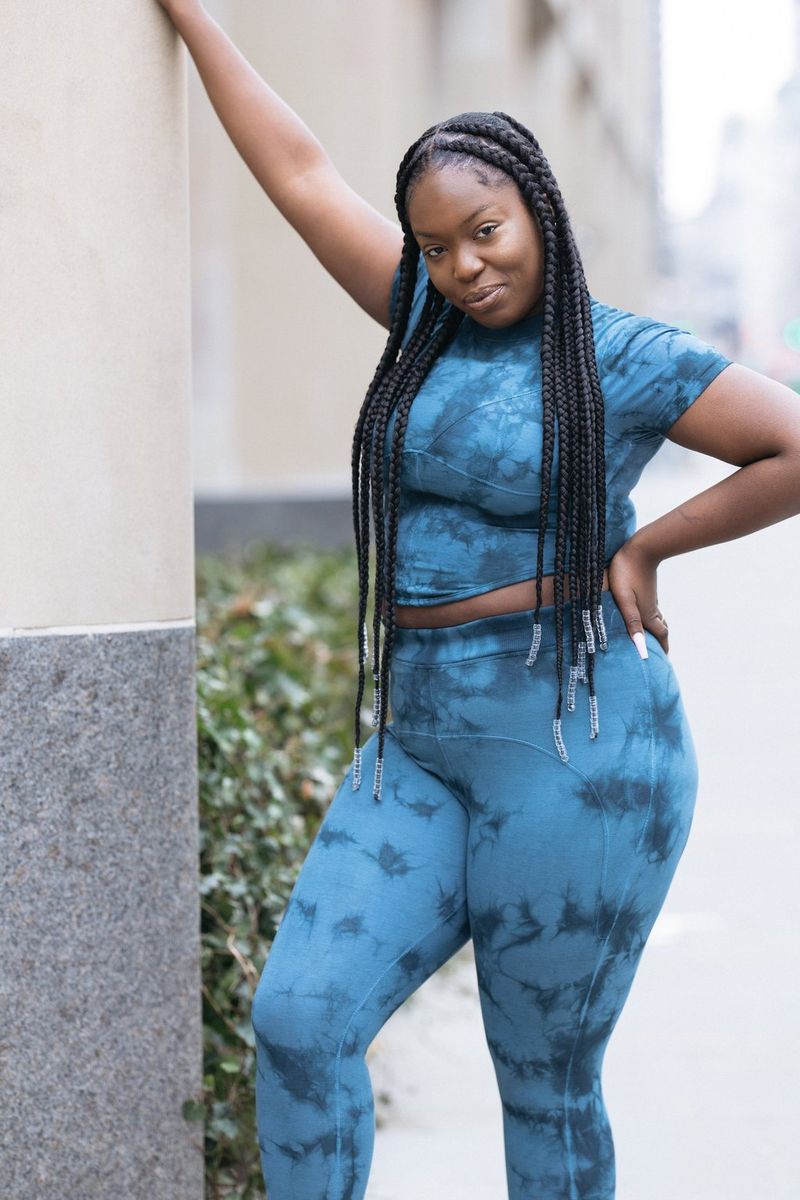 אישה נשענת על קיר, לובשת חולצה כחולה בצבעי בטיק (Tie-dye) וחותלות תואמות.