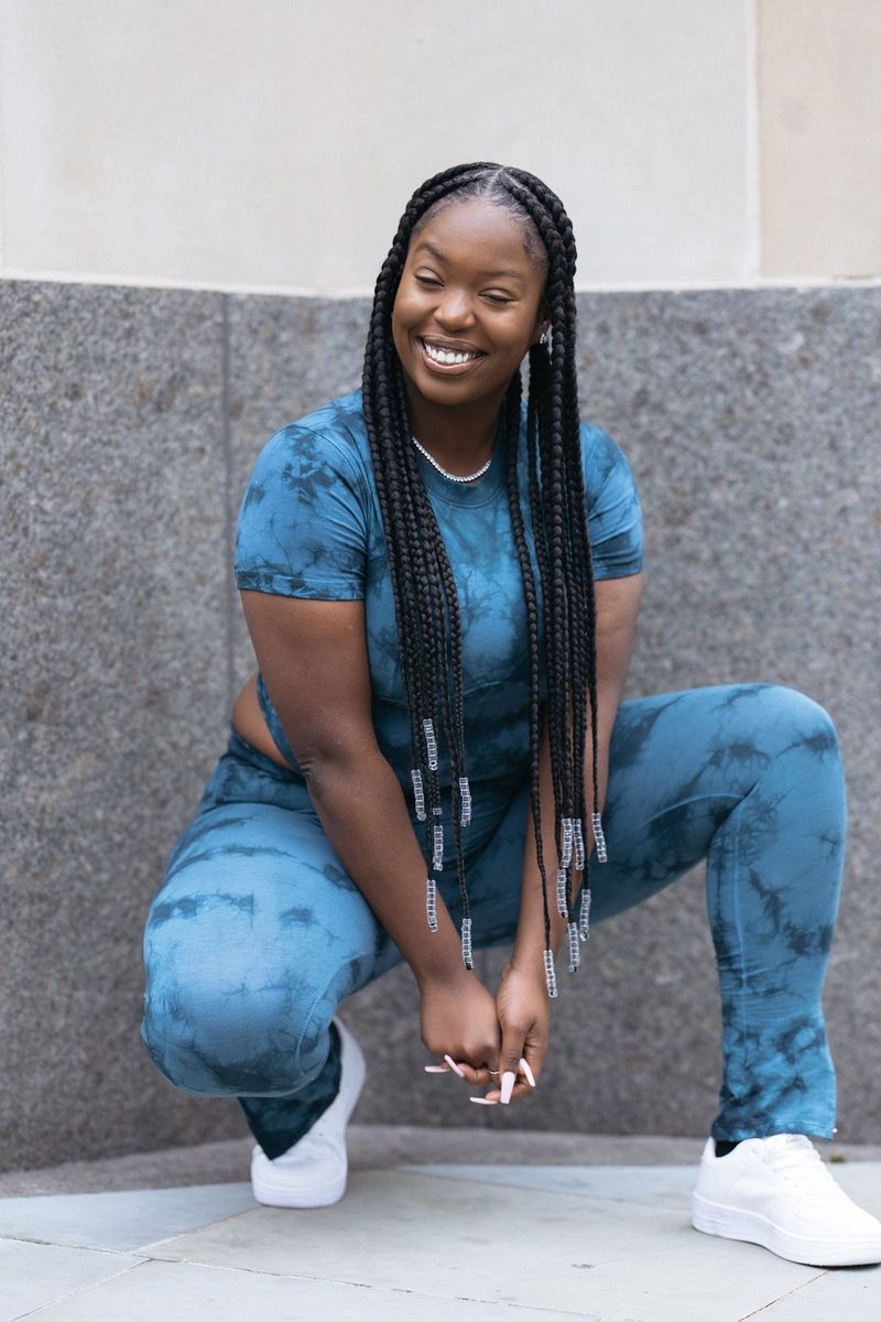 אישה מתכופפת, בחולצת בטיק (Tie-dye) כחולה וחותלות תואמות, עם נעלי ספורט לבנות.