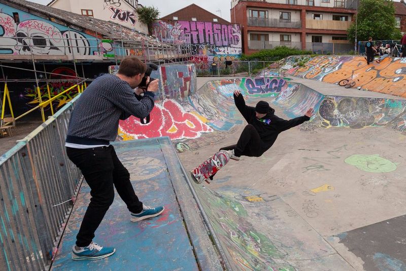 Un uomo in piedi in cima a una rampa che fotografa uno skateboarder.