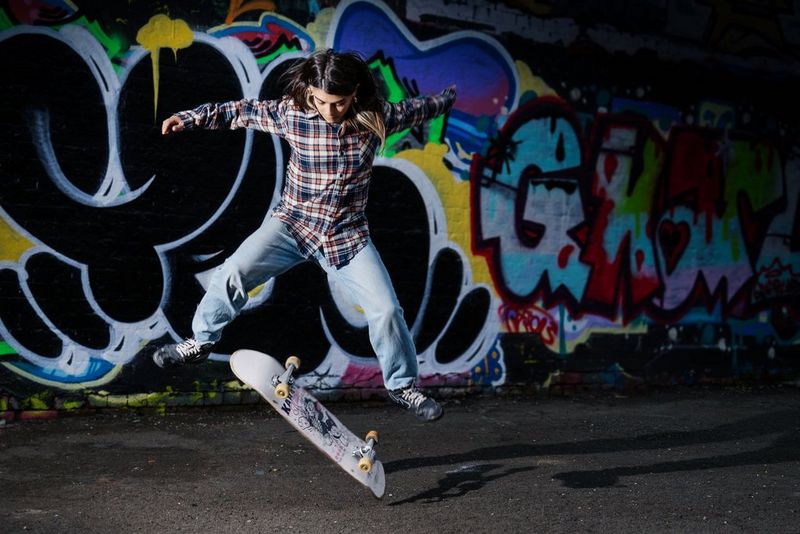 Una skateboarder che esegue un trick davanti a un muro ricoperto di graffiti.