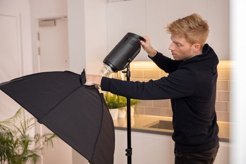 Een man die volledig in zwart is gekleed, past een grote studiolamp aan in een keuken.