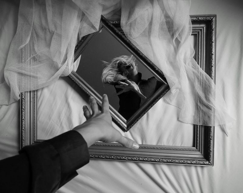 Črno-bel posnetek odseva ženske z iztegnjeno dlanjo v zrcalu.