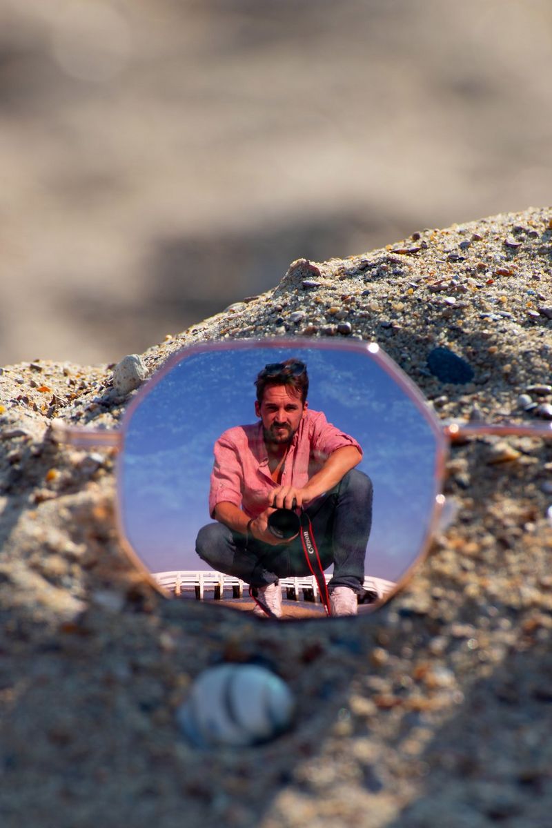 Šestkotna sončna očala z odsevom avtoportreta moškega, ki čepi na skali.