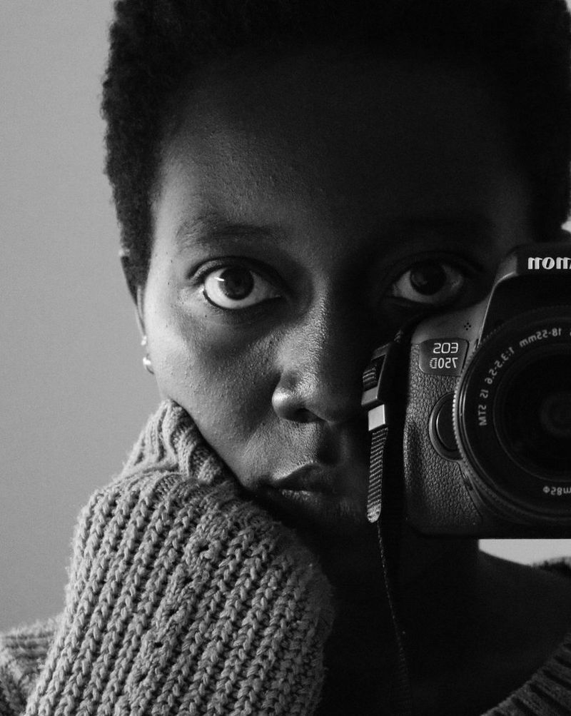 Črno-bel selfi ženske, ki gleda v objektiv fotoaparata, ki ga drži pred obrazom.