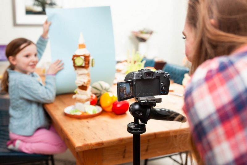 Een klein meisje houdt een stuk blauw papier omhoog achter een toren van eten in de vorm van de Big Ben.