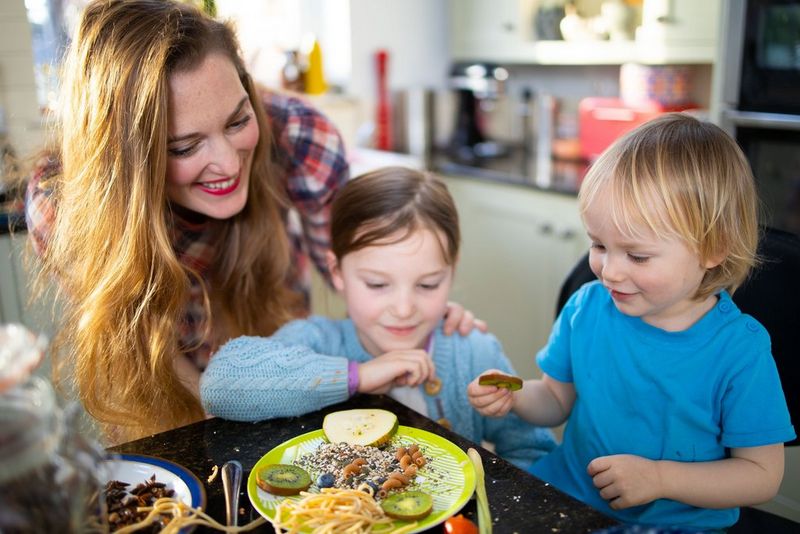 Een moeder en haar twee kinderen die eten in de vorm van een gezicht op een groen bord neerleggen.