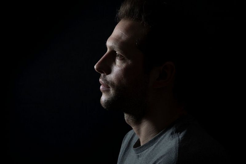 Moški, gledan v profil, z osvetljenim obrazom. Zadnji del glave in ostali del okvirja sta v senci.