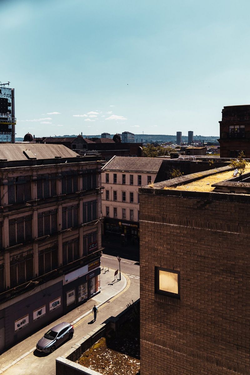 Shot from above, a car drives down a city street flanked by tall buildings, in a photograph taken on a Canon EOS R8 by Andres McNeill. 