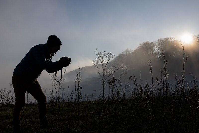 A landscape photographer crouches to capture plants in the early-morning sun. 