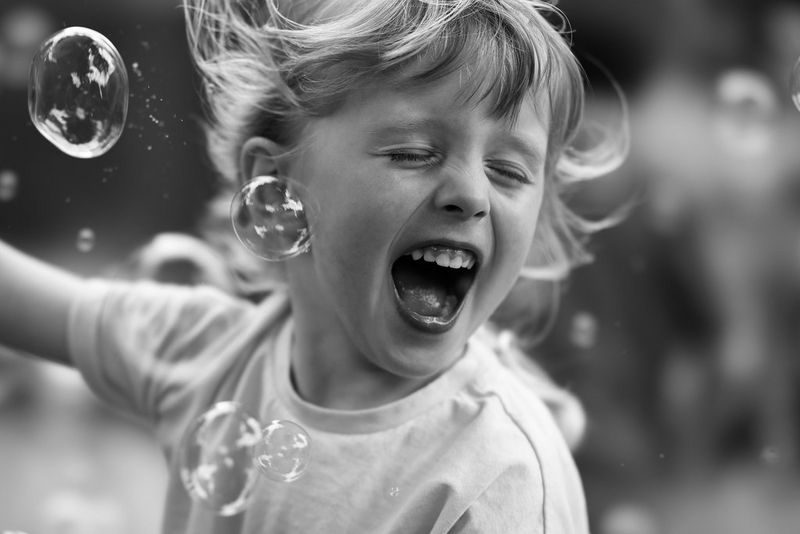 Черно-белый снимок смеющегося ребенка, играющего с пузырьками.