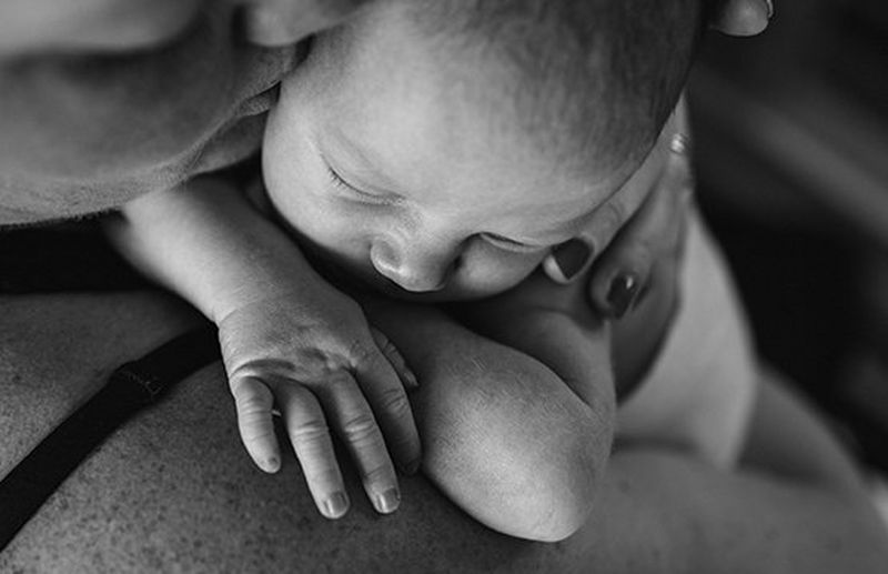 A black and white close-up shot of a mother kissing a sleeping baby she is holding to her shoulder.