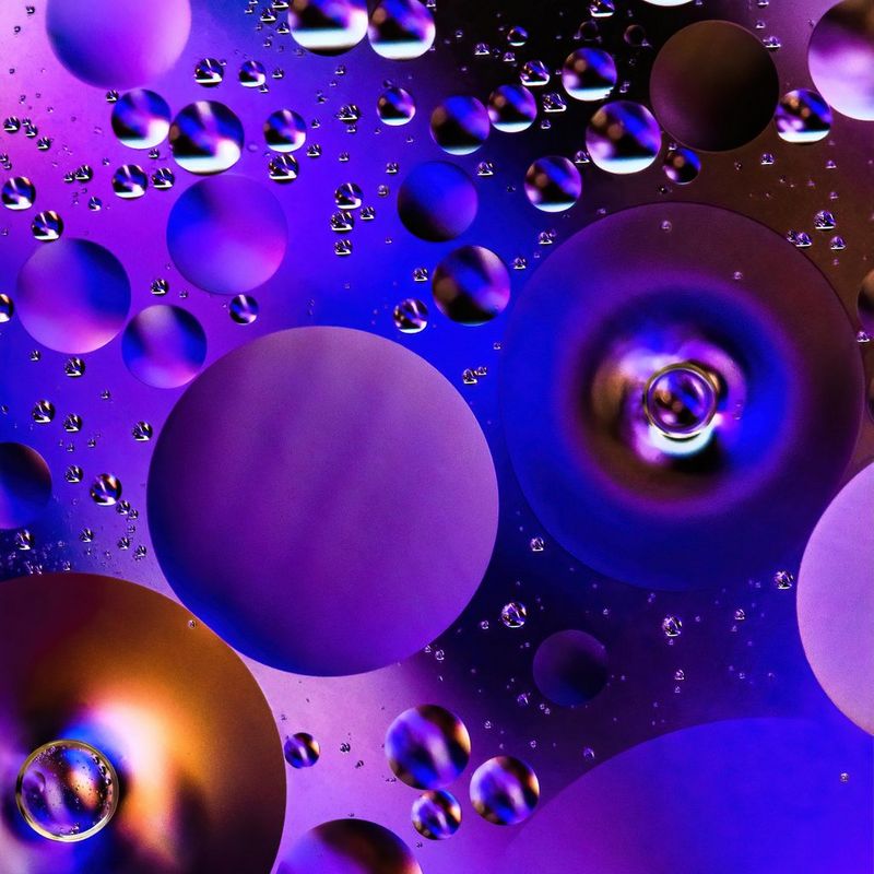 Una fotografia macro di olio sull'acqua, che crea gocce circolari di colore viola.