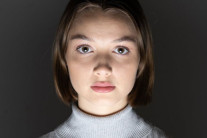 Portret van een vrouw in een grijze coltrui, belicht van onderaf.