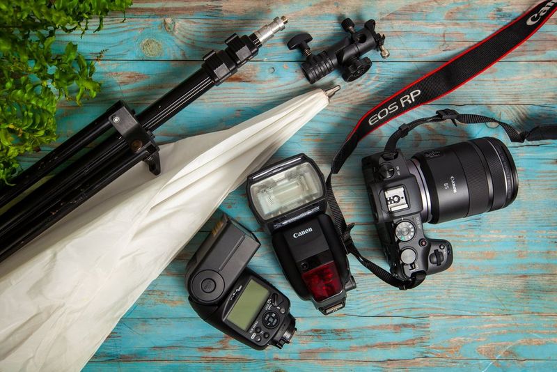 Een Canon EOS RP, met twee Canon Speedlites, een statief en een witte paraplu, uitgestald op een houten tafelblad.