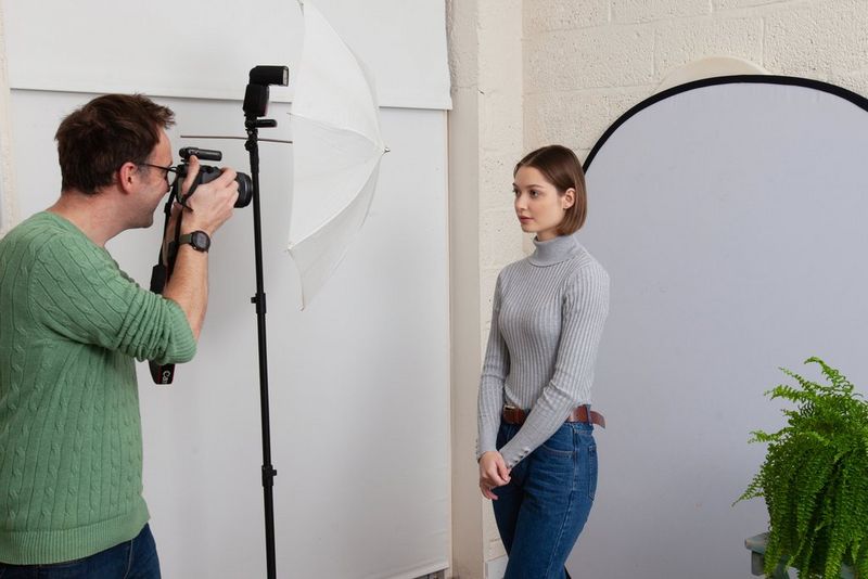 Een man die portretten fotografeert in een thuisstudio, met een grijze achtergrond en een witte paraplu om het licht van de flitser te verzachten.