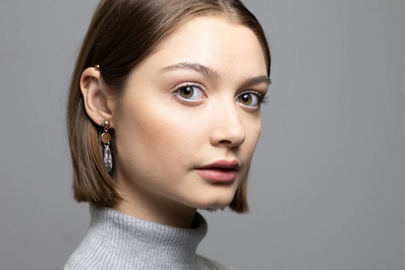 Een portret vanaf de zijkant van een jonge vrouw in een grijze coltrui die naar de camera kijkt.