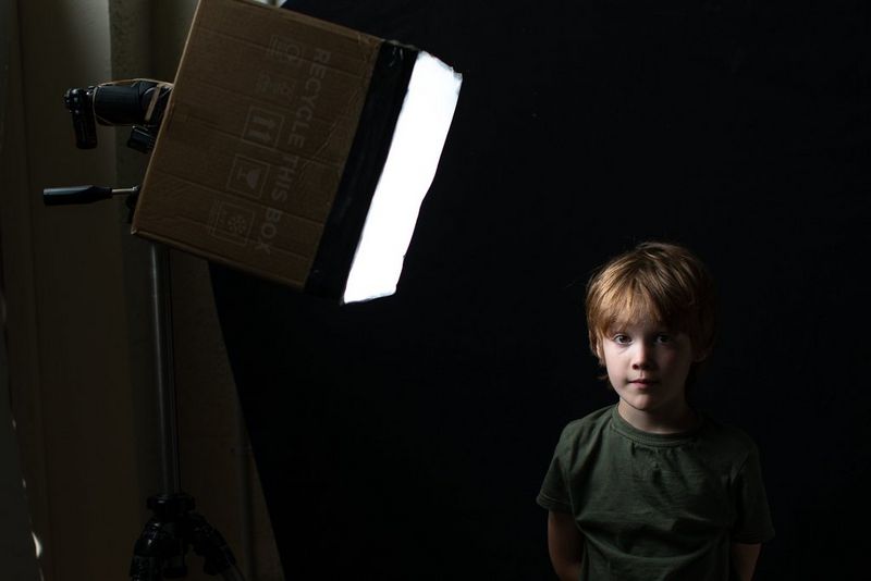 Вспышка Speedlite на штативе обеспечивает мягкое освещение мальчика через картонную коробку.