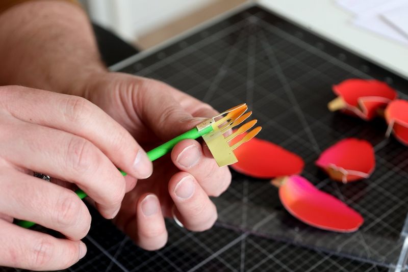 A pair of hands carefully folds the inner part of a papercraft flower.