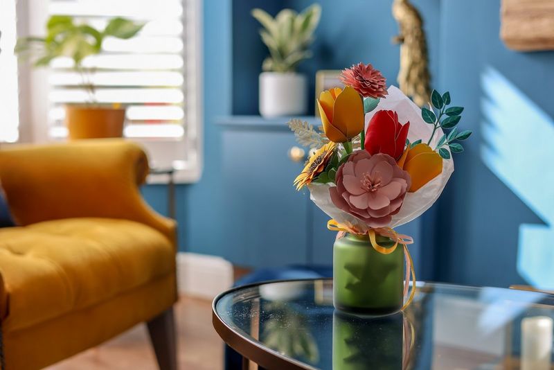 A colourful bunch of papercraft flowers sit in a vase in the centre of a living room.