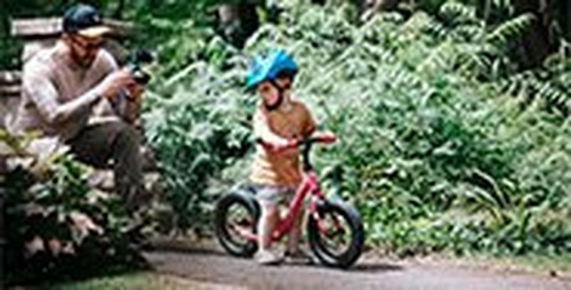 Stef Michalak crouching on a path with a Canon EOS M50 to film his son's first ride on a balance bike.
