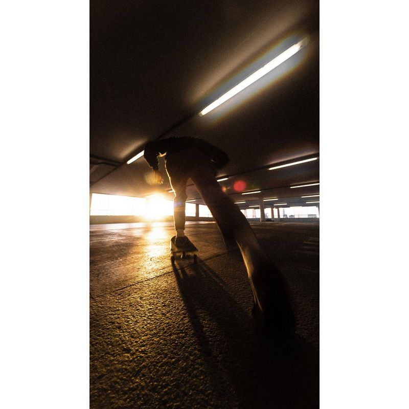 Een skateboarder die zich afzet in een donkere parkeergarage met meerdere verdiepingen.