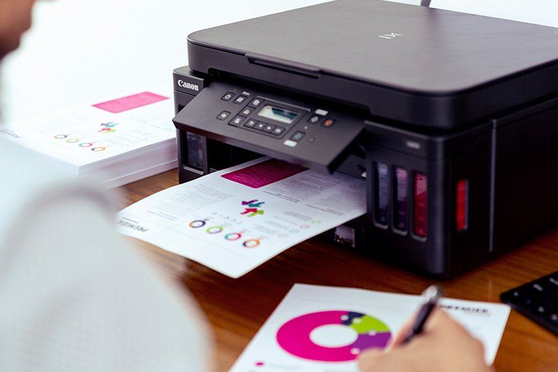 A man sits in front of a PIXMA G6040 Canon printer making notes on a printout.