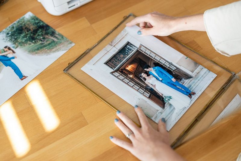 Ruka aranžuje svadobnú fotografiu v ráme na drevenom povrchu.