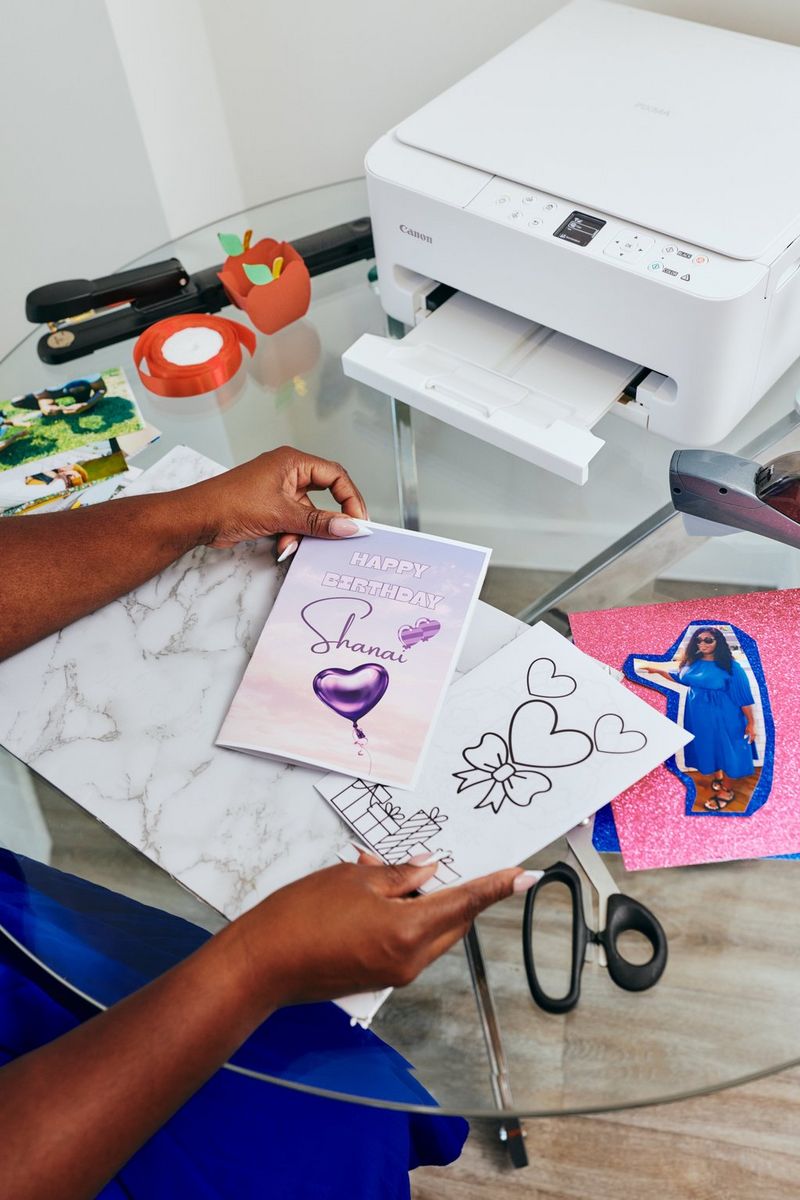 Een zelfgemaakte verjaardagskaart die op een glazen tafel in elkaar wordt gezet. Op deze tafel liggen verschillende papieren elementen en staat een Canon PIXMA-printer.