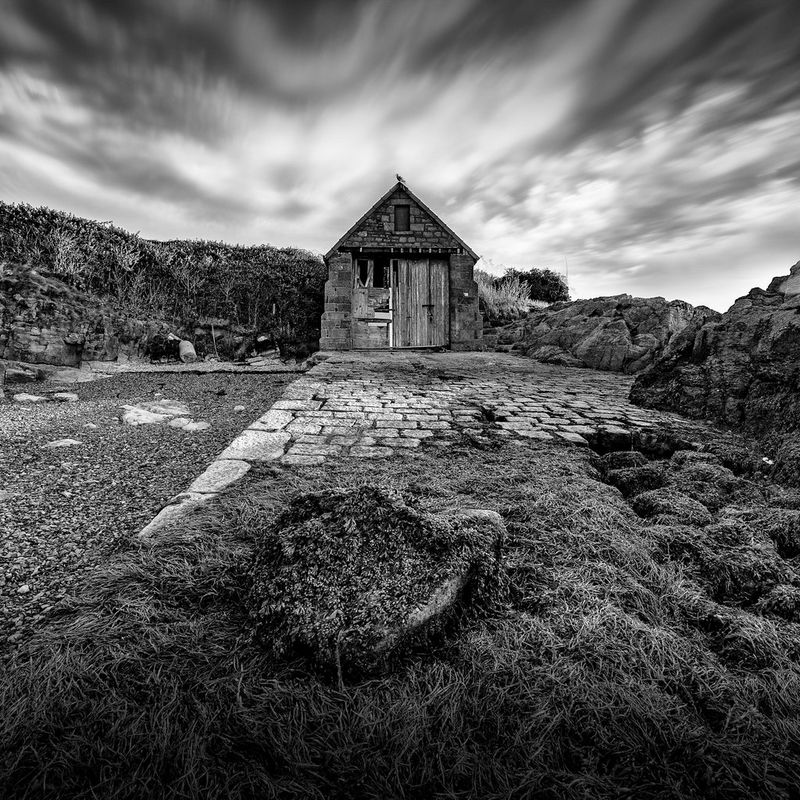 Una rimessa per barche in rovina è catturata insieme a nuvole che sembrano vorticare sopra di essa.