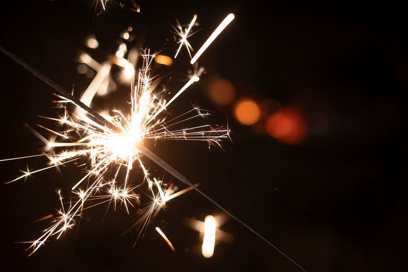 A bright sparkler burning down, throwing sparks in all directions.