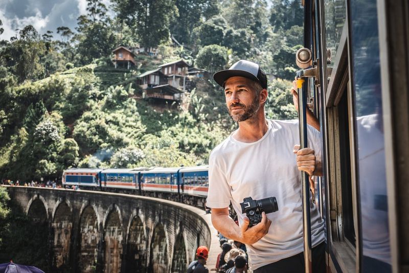 Фотограф Мартин Биссиг держит в руках камеру Canon EOS R10, выглядывая из окна поезда на Шри-Ланке.