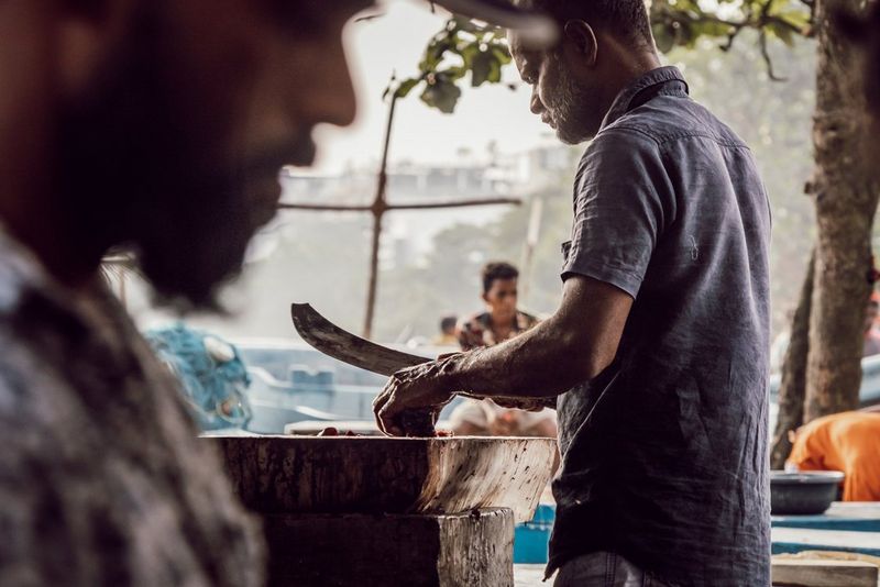 A person chops fish on a wooden block at a market stall. Taken by photographer Martin Bissig on a Canon EOS R10 with a Canon RF-S 18-150mm F3.5-6.3 IS STM lens.