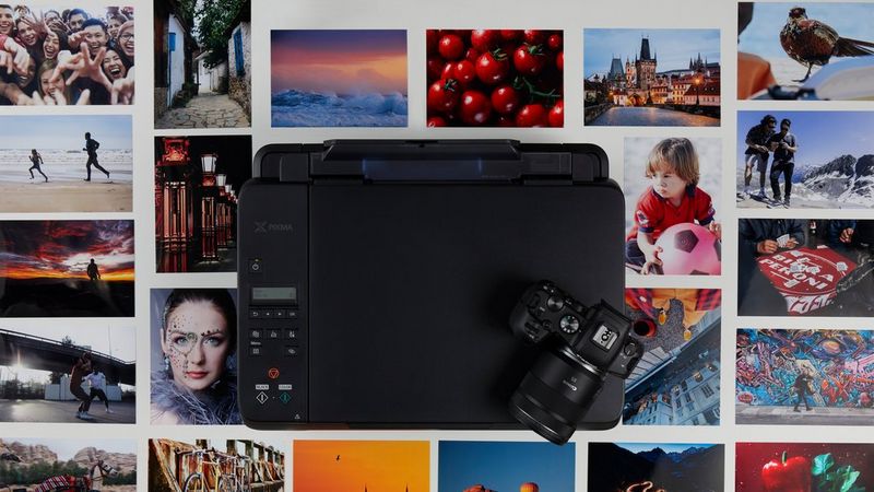 Een Canon PIXMA G650 met een camera er bovenop, omringd door geprinte foto's.