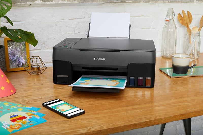 Een Canon PIXMA G3520-printer op een bureau naast een smartphone.