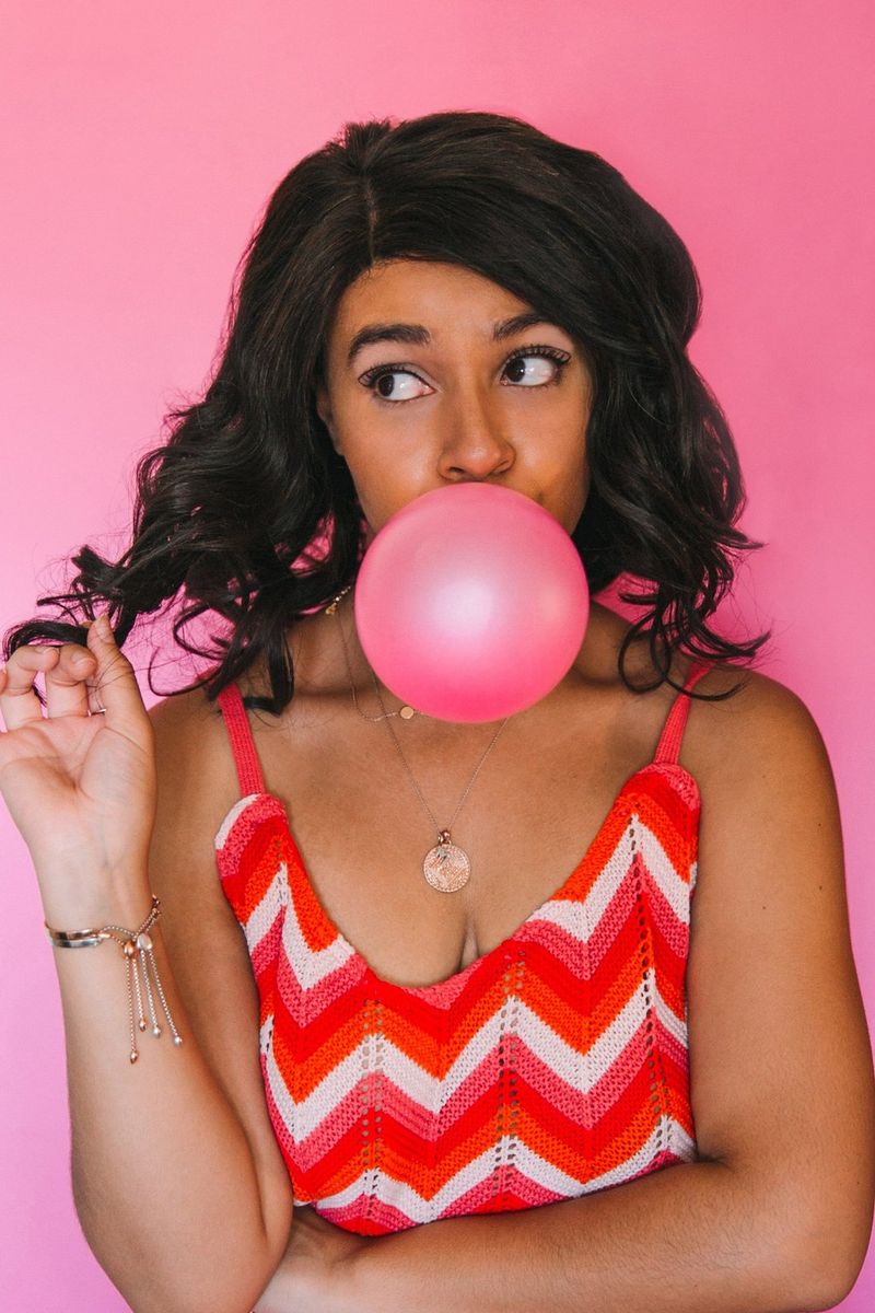 Portrét mladé ženy, která si kroutí vlasy a vyfukuje něco, co vypadá jako bublina ze žvýkačky.