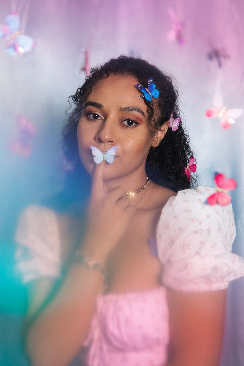 Žena v bílých šatech s papírovými motýlky ve vlasech a na rtech.