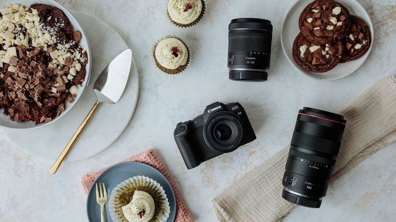 Een Canon EOS R8-camera en een selectie Canon RF-lenzen van bovenaf getoond, omringd door cakes, koekjes en ingrediënten.