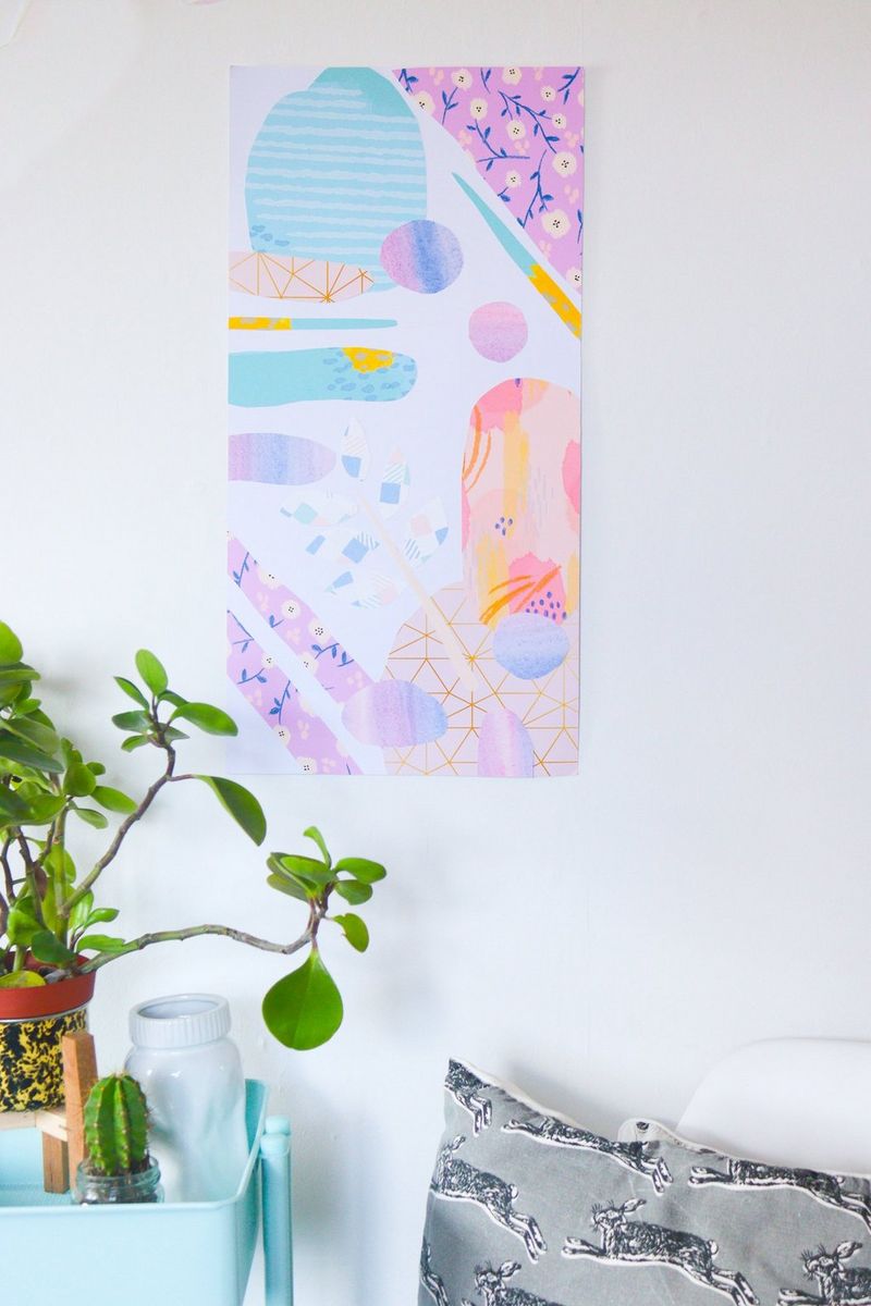A pastel-hued abstract artwork hangs on a white wall. Below it are a pot plant and a grey cushion.