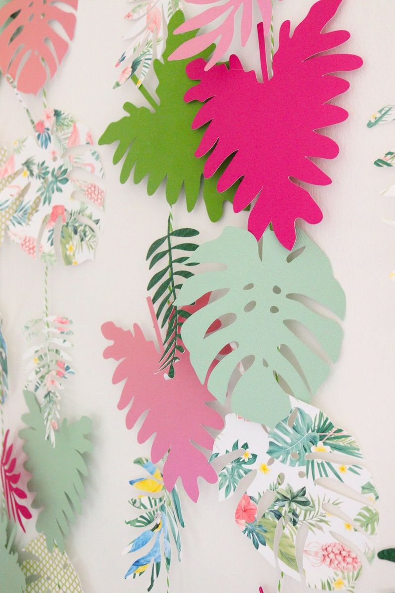 A wall hanging made of tropical leaf shapes, cut out of colourful paper in pinks and greens and tropical prints.