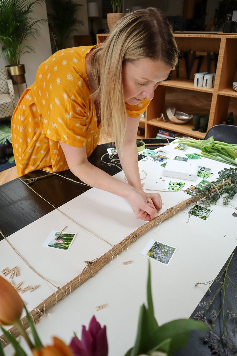 A woman in a yellow dress leans over a table, tying lengths of jute around a branch.