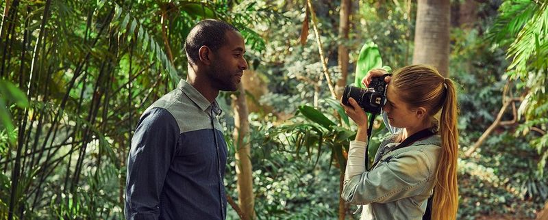 A camera being held above green leaves, showing the rear display. 