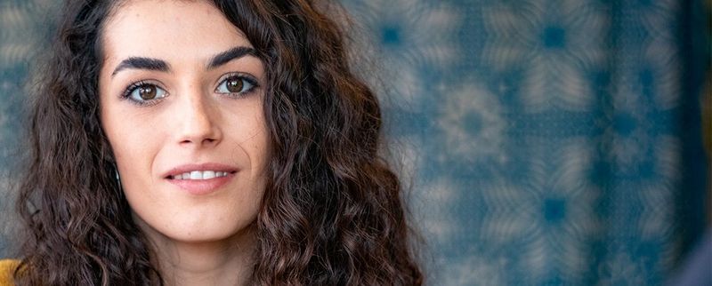 Portrait of a woman with dark hair and a red top, against blurred green plants.