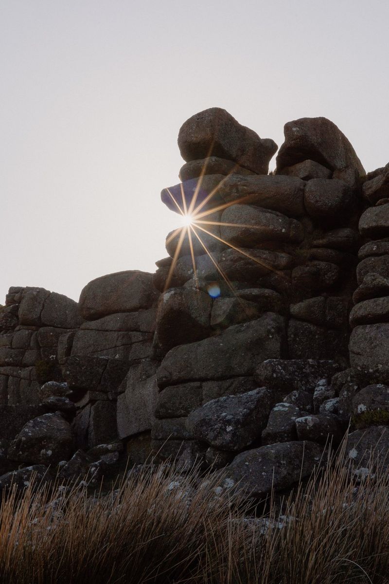 На этом снимке, сделанном в условиях слабого освещения, изображены лучи солнечного света, пробивающиеся сквозь отдельно стоящее скалистое образование.