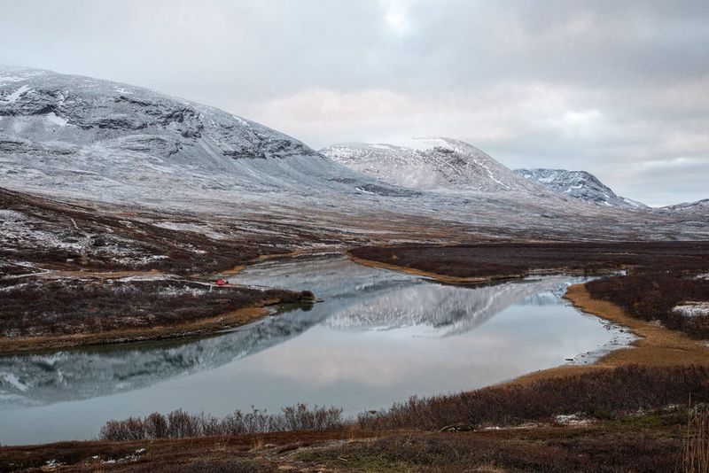 На этой эффектной пейзажной фотографии изображены покрытые снегом горные вершины, отражающиеся на водной глади большой реки.