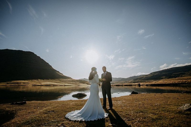 A newlywed couple standing in a wild, unspoilt landscape, as the low sun casts long shadows on the ground.