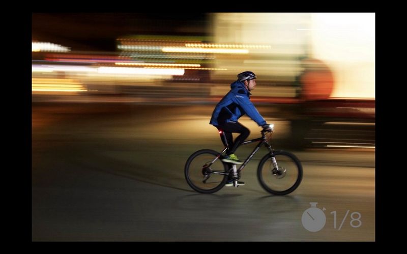 A man cycling down a street with the lights around him blurred.